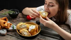 Žena jí plněné palačinky u dřevěného stolu, domácí jídlo, večeře