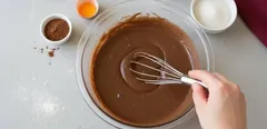 Míchání čokoládového těsta v míse na pečení s kakaem a vejcem na stole.