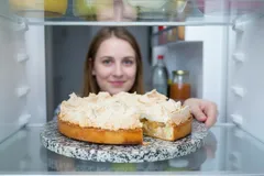 Žena bere dort z lednice, pohled z vnitřku lednice, dort s krémem na mramorové podložce.