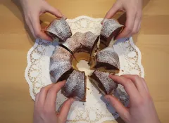 Domácí bábovka na talíři, lidé si berou jednotlivé kousky dezertu rukama.