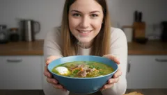 Žena držící misku s tradiční polévkou s vejcem a zeleninou v moderní kuchyni.