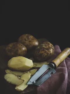 Loupané a neloupané brambory na dřevěném stole s výraznou žlutou barvou