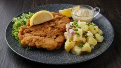 Smažený řízek s bramborovým salátem, citronem a tatarskou omáčkou na talíři